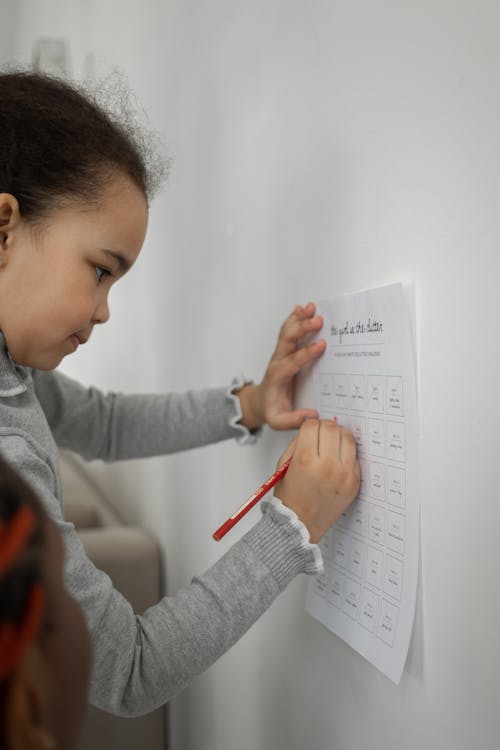 Serious ethnic little kid writing on worksheet near wall