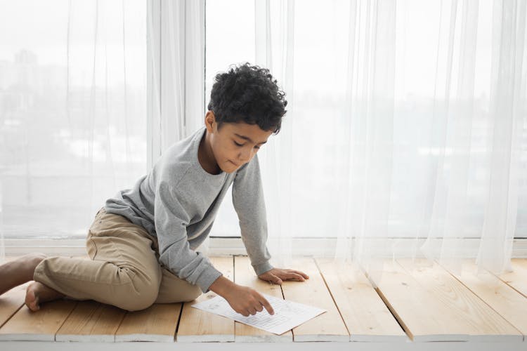 Attentive Black Boy Reading Paper On Windowsill