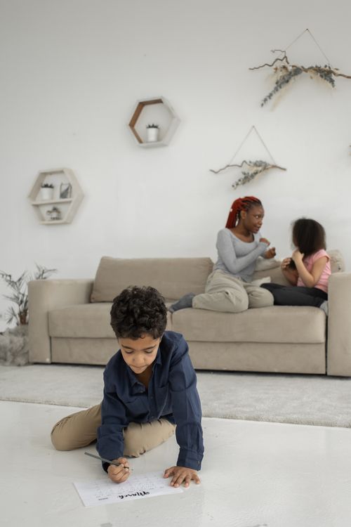 Free African American mother and daughter sitting on sofa while discussing details and boy sitting on floor near couch Stock Photo