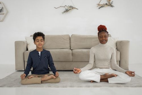 Free Full body of happy African American woman and cute boy meditating in Lotus pose together while sitting on floor in modern apartment with sofa Stock Photo