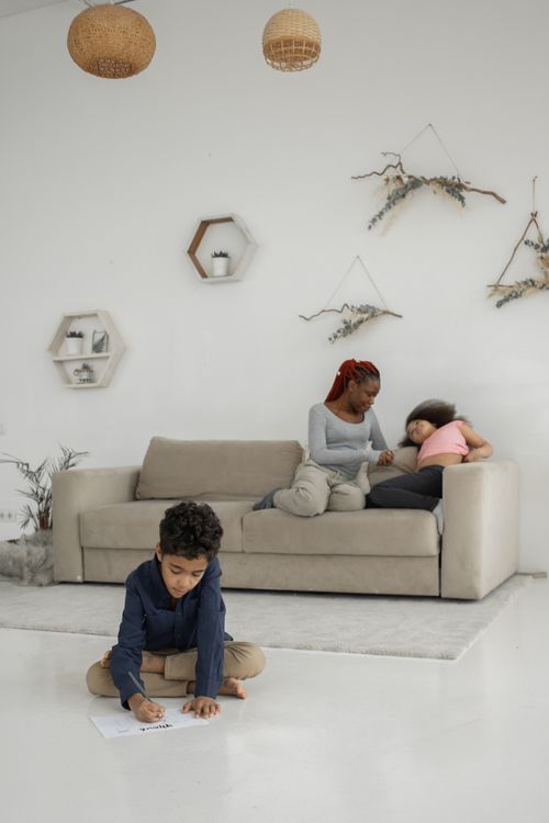 Free Full body of black woman and little girl sitting on sofa near boy sitting on floor in modern room Stock Photo