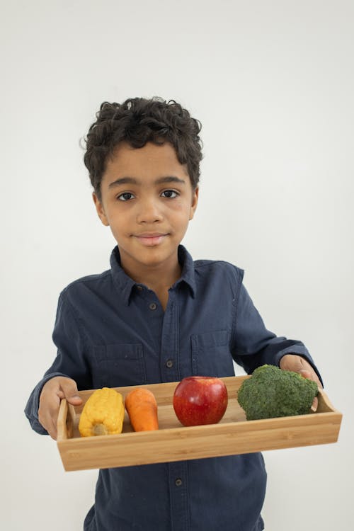 Smiling black kid demonstrating tray with colorful healthy vegetables