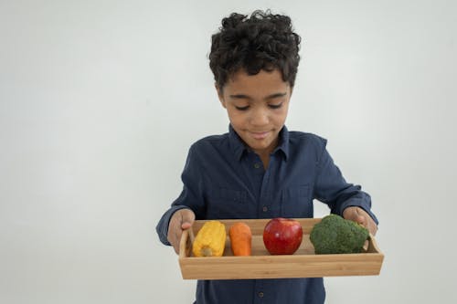 Happy ethnic kid holding wooden tray with colorful raw products