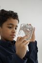Crop concentrated ethnic little bot with curly dark hair in casual clothes playing with transparent slime against white background