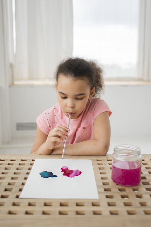 Free Ethnic little girl blow water coloring paint on paper at table Stock Photo