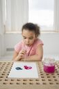Ethnic little girl blow water coloring paint on paper at table