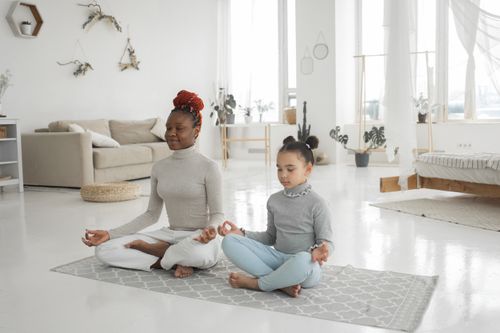 Free Full body of young African American woman with cute little daughter sitting in carpet with closed eyes and meditating in Lotus pose at home Stock Photo