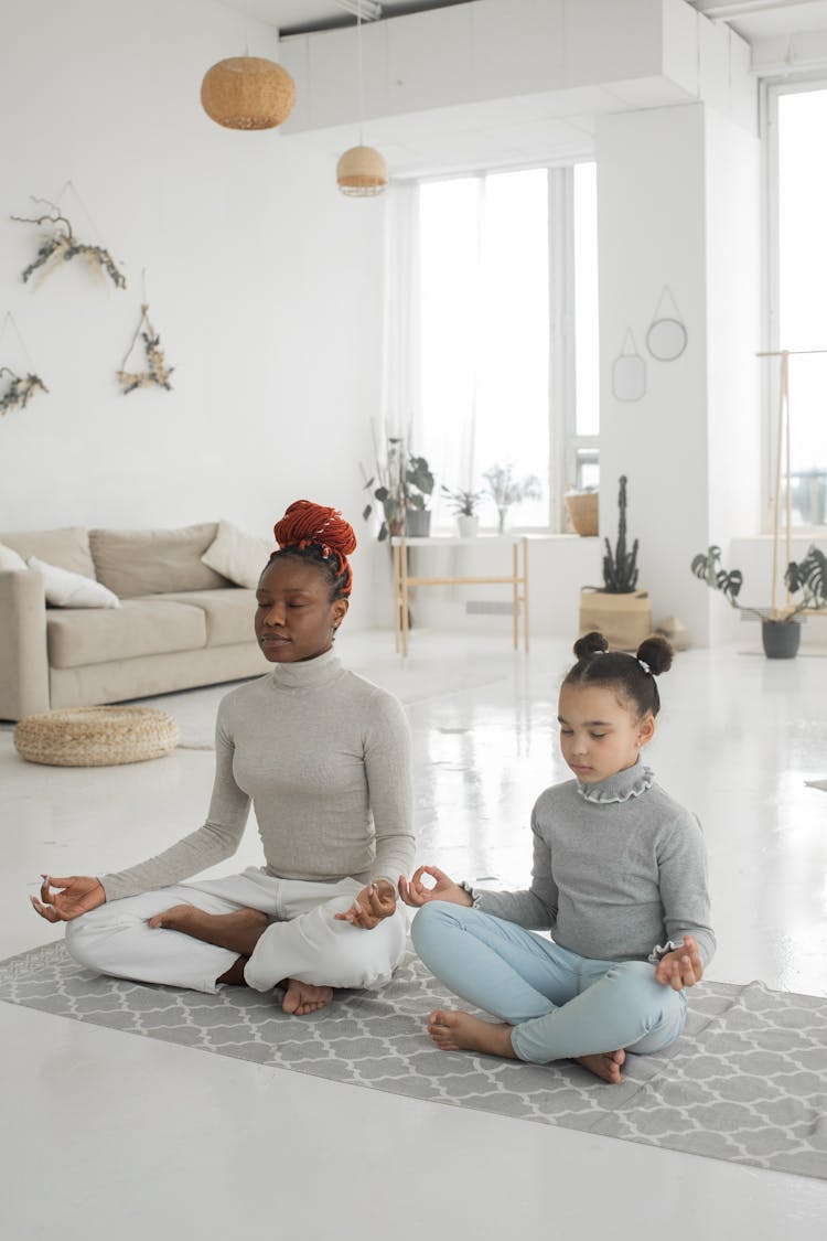 Calm African American Woman With Daughter Meditating With Closed Eyes In Living Room