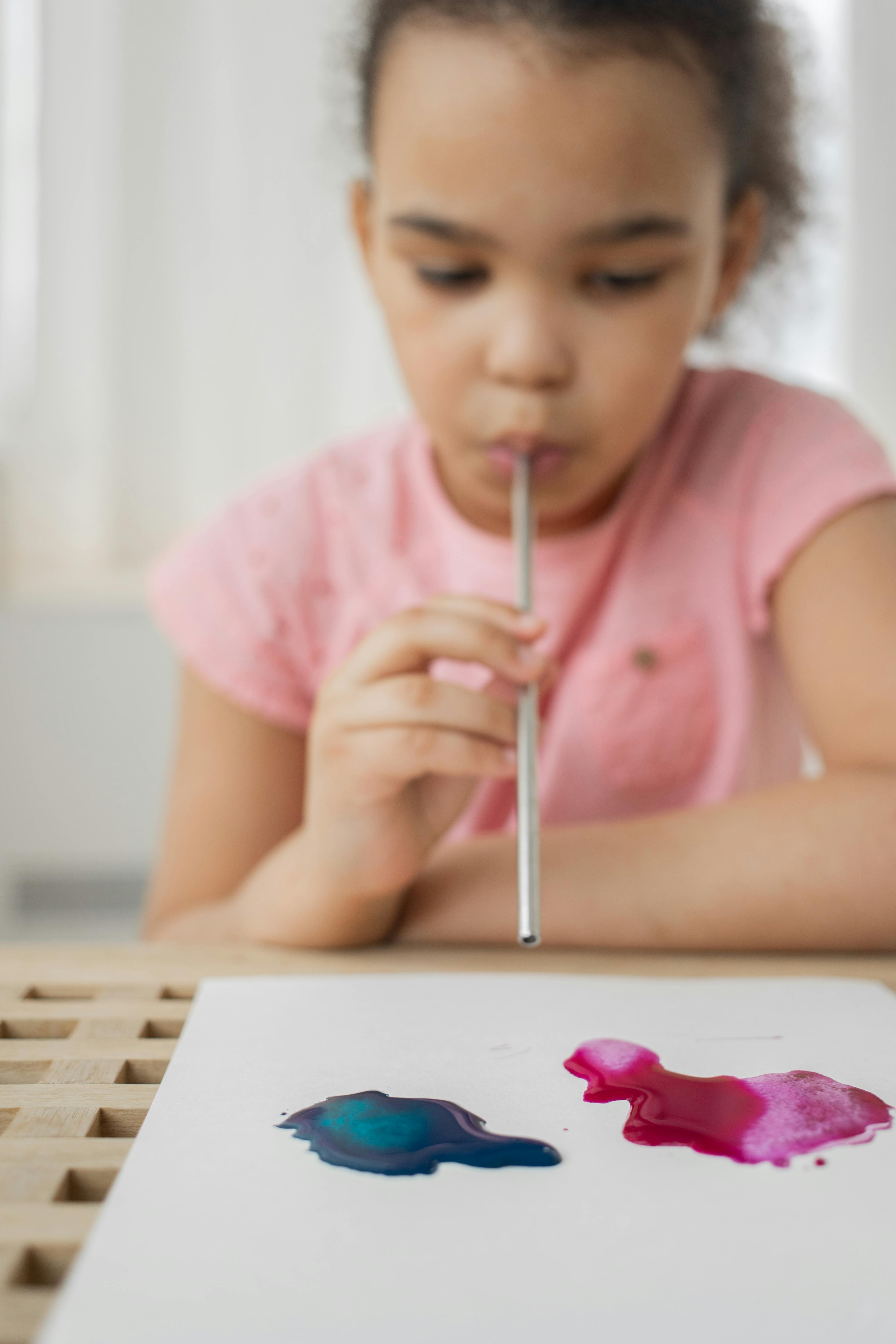 talented little ethnic girl painting with aquarelle and straw on paper