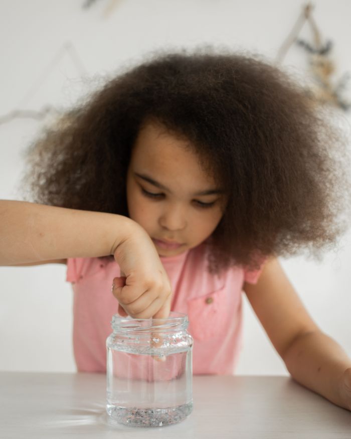 A girl dipping her finger into a jar of water during a simple experiment