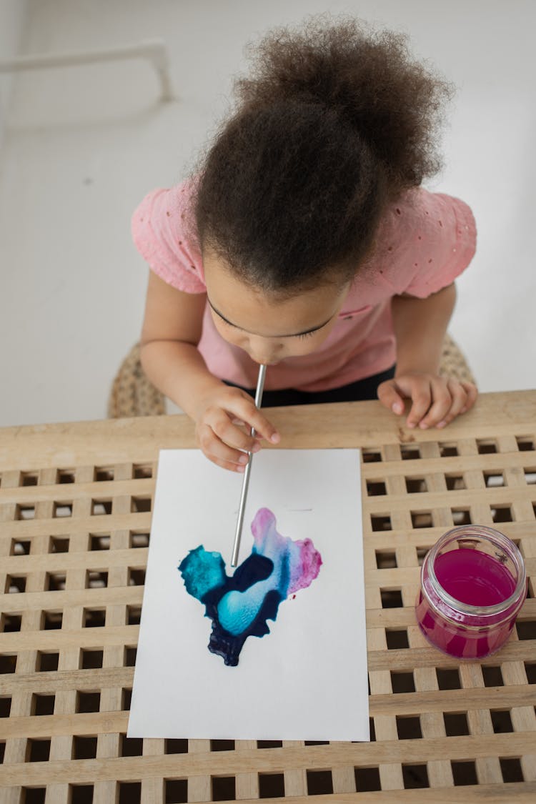 Little African American Kid Blow Painting On Paper With Straw And Aquarelle