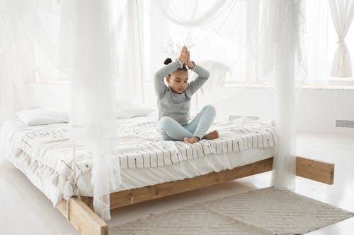 Cute ethnic kid practicing meditation in Padmasana pose on bed