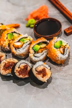 Close-up of colorful sushi rolls with avocado, sauce, and chopsticks on a marble surface.