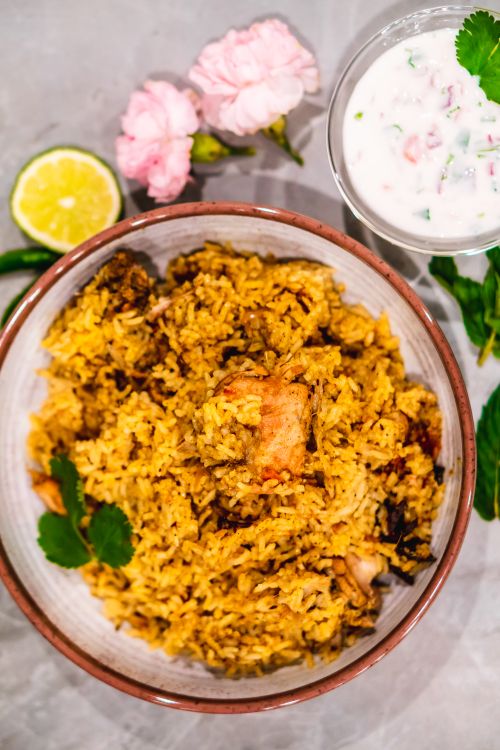 Chicken biryani in a bowl with raita and lemon alongside