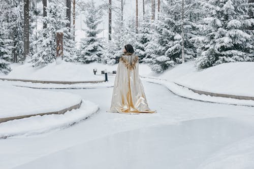 Woman Wearing Cape Walking on Snow Covered Pathway
