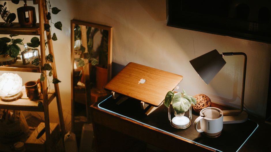 Warmly lit home workspace featuring a laptop, lamp, and green plants on a desk.