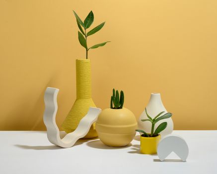 Modern minimalist setup with succulents in yellow vases on a white table against a matching backdrop.