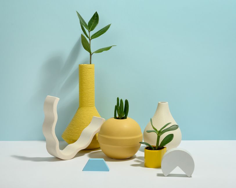 Memphis decor style interior — A minimalist display featuring various decorative vases with succulent plants on a light blue background.
