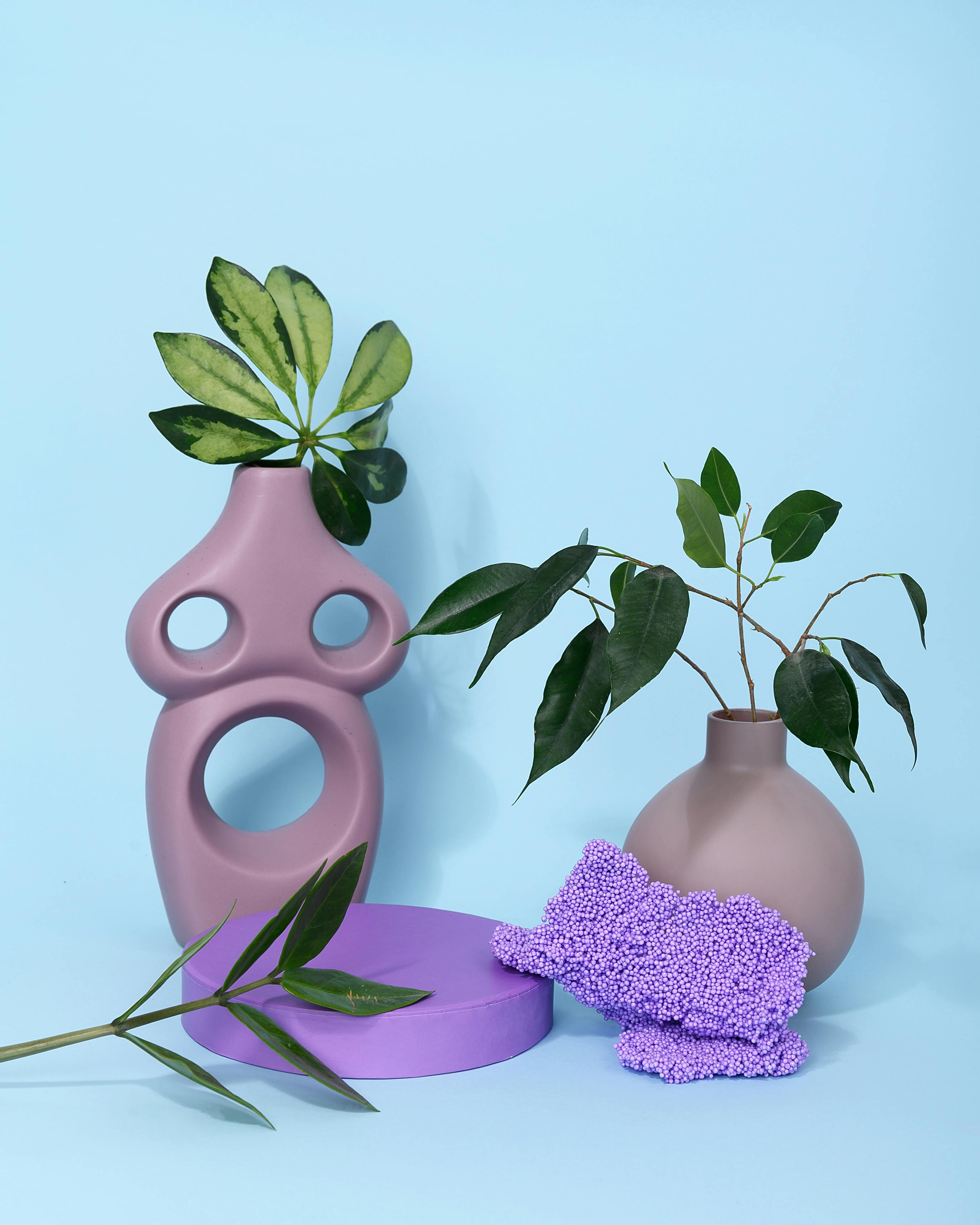 Stylish modern vases with green leaves on a pastel blue background, ideal for chic decor settings.