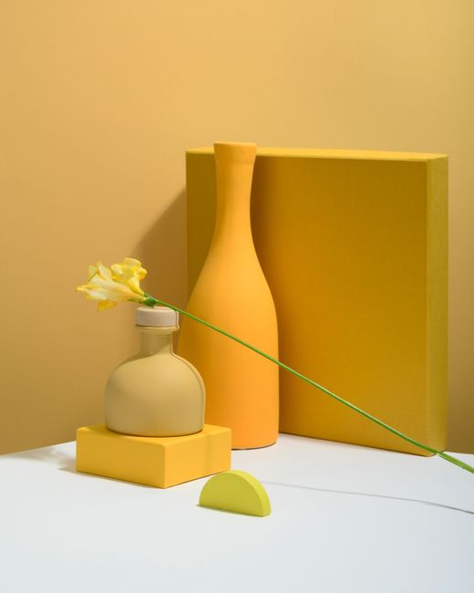 Minimalist yellow still life with vases and flowers on a gradient background.