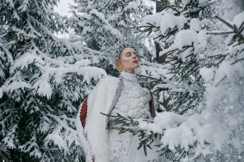 Woman in winter costume with crown surrounded by snow-covered trees