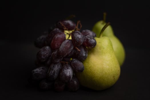 A vibrant close-up of fresh pears and grapes against a dark backdrop, highlighting natural texture and color.
