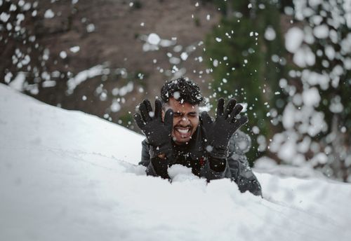 Free An adult having fun in the snow with winter gloves, creating a lively and joyful winter scene. Stock Photo