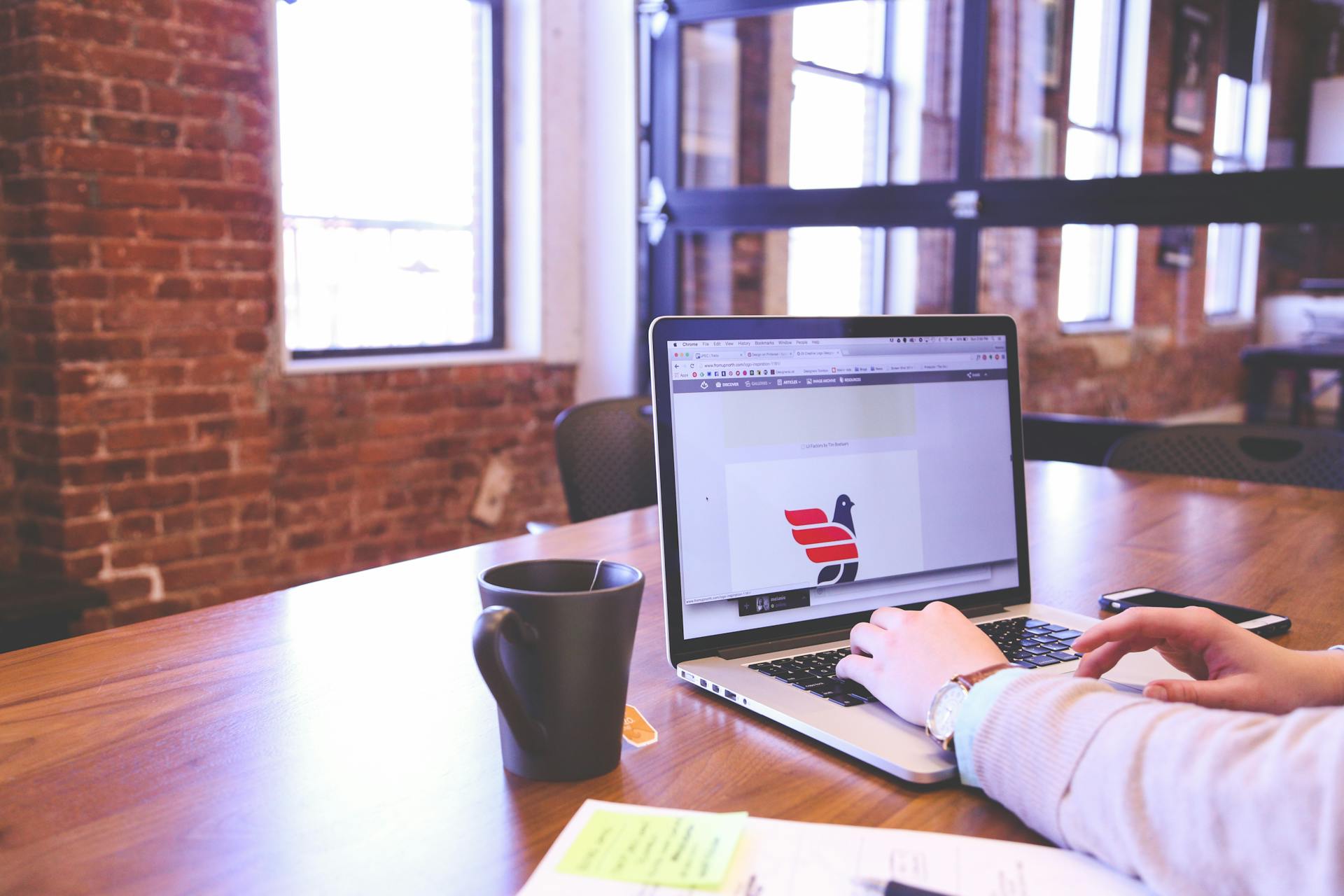 Person working on laptop in a trendy brick-walled office with modern aesthetics.