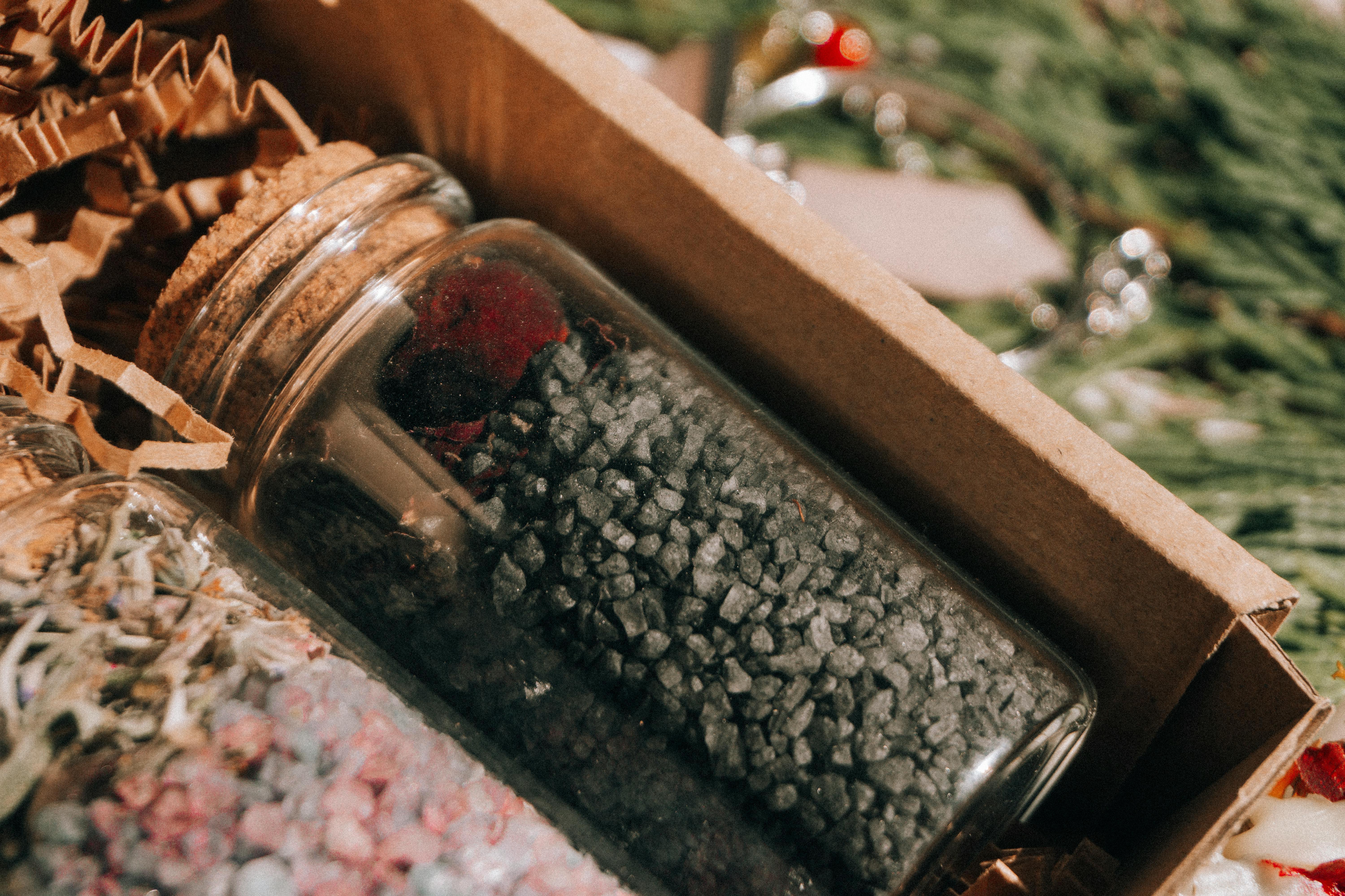 Detailed shot of glass jars containing different spices, including black salt, in a rustic cardboard box.