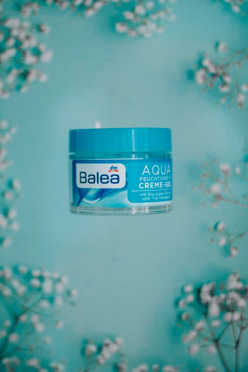 Free Top view of glass jar with moisturizing face cream placed on blue background with abundance of sprigs with small flowers Stock Photo