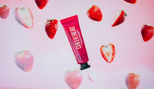 Red tube with gel cream blush with strawberry flavor for daily beauty routine and makeup application placed on pink background