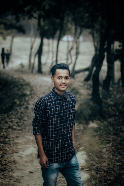 Free A young man in a plaid shirt pose in a wooded area, exuding a casual yet fashionable look. Stock Photo