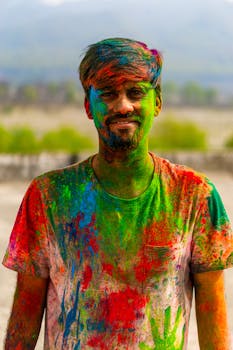 Smiling man covered in colorful Holi powder outdoors during Indian festival.