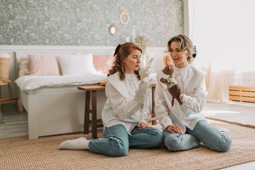 Free Two women enjoying a puppet show in a cozy bedroom setting. Stock Photo