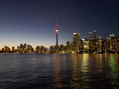 A stunning view of Toronto's skyline featuring the iconic CN Tower reflecting on Lake Ontario at night.