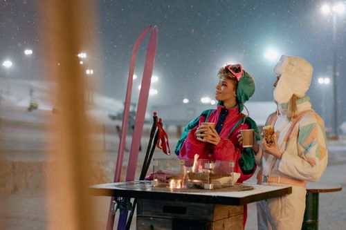 Free Women enjoying warm beverages by a fire outdoors on a snowy winter night. Stock Photo