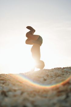 A person performs a handstand on a sunny beach, creating a striking silhouette.