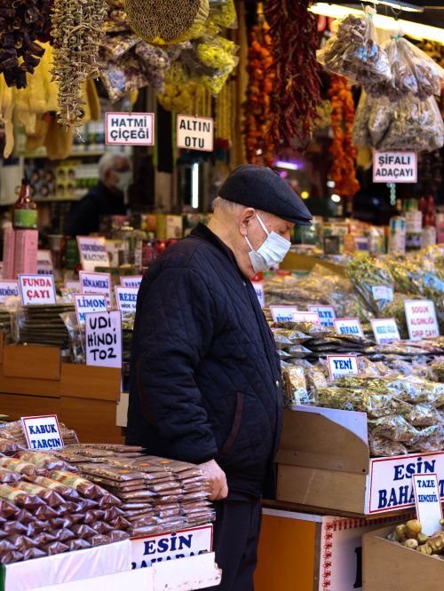 Free Elderly man wearing a face mask browsing a spice stall in a bustling Bursa market. Stock Photo