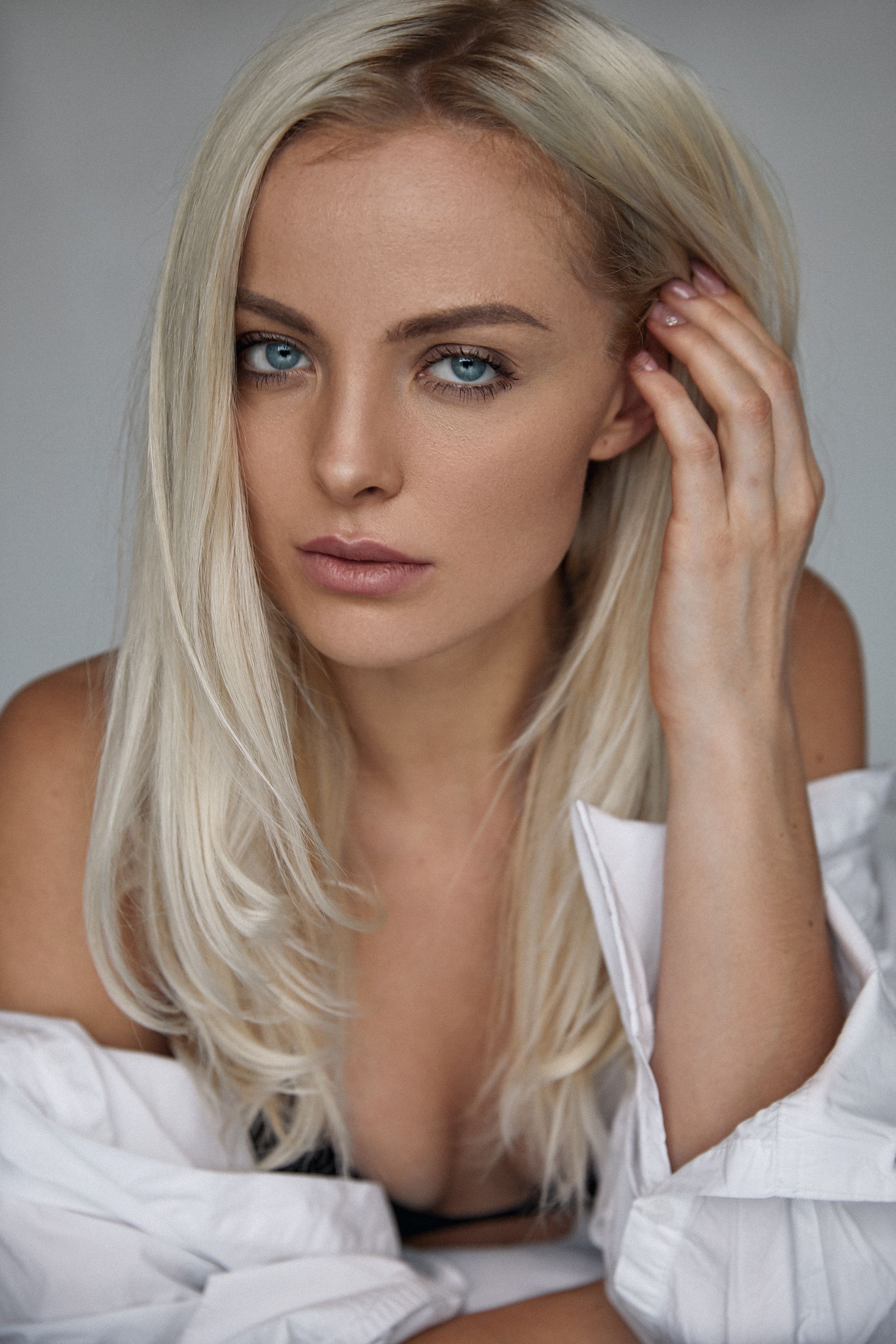 Close-up portrait of a blonde woman with blue eyes, hand on hair, and stylish pose.
