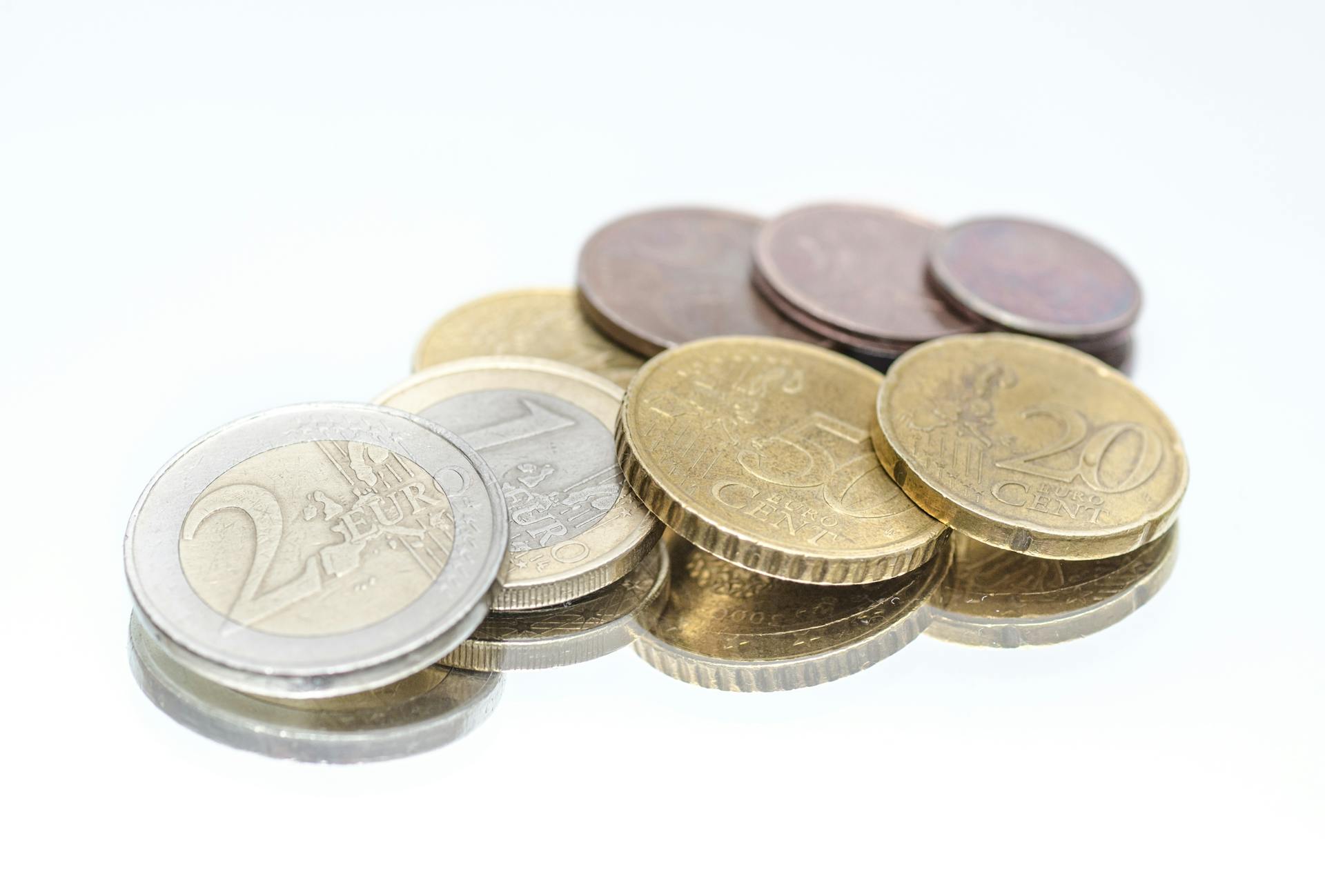 Close-up of Euro coins in different denominations placed on a shiny reflective surface.