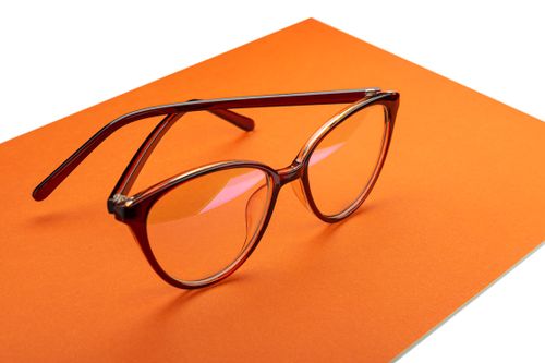 Free Close-up view of trendy eyewear with brown frames placed on an orange background, showcasing elegant design. Stock Photo