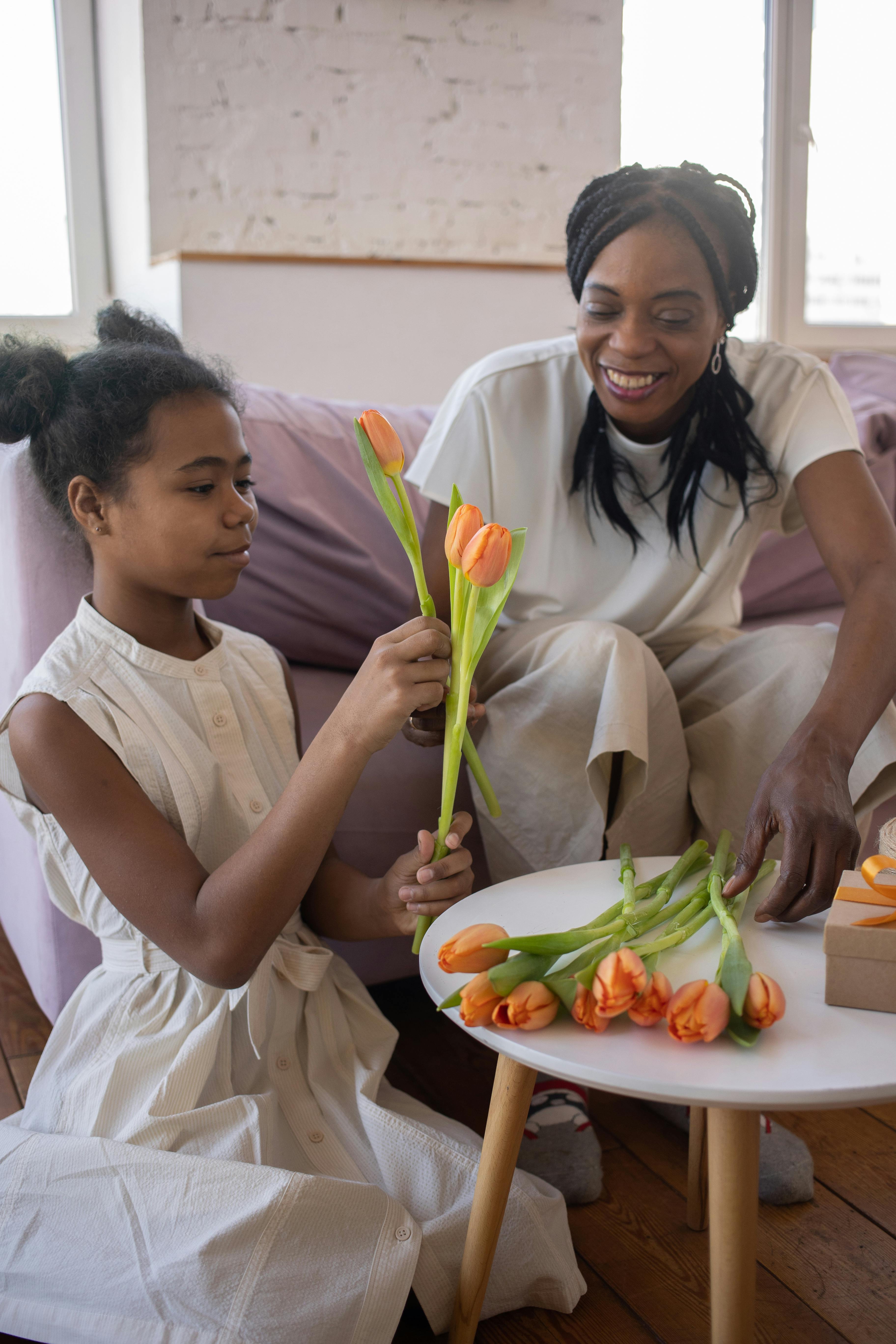 a woman sitting on the couch while looking at her daughter holding flowers