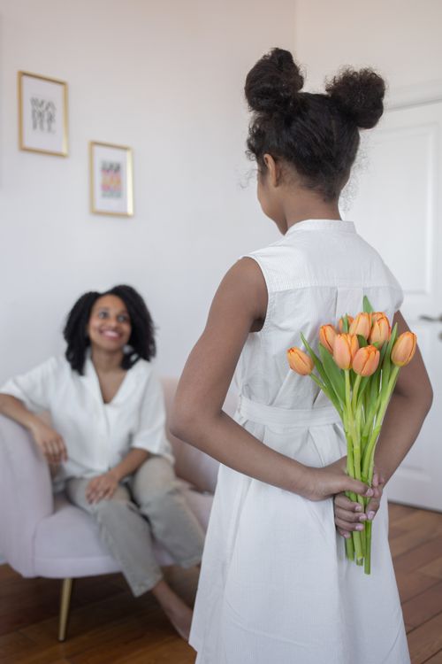 Free A young girl surprises her mother with tulips, creating a heartwarming indoor scene. Stock Photo
