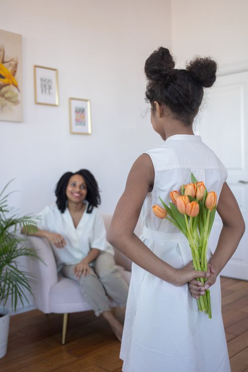 Free A young girl surprises her mother with tulips in a bright, indoor setting. Stock Photo