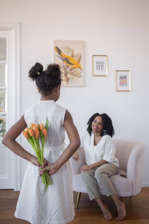 Free A touching Mother's Day moment as a daughter surprises her mother with a bouquet of tulips indoors. Stock Photo