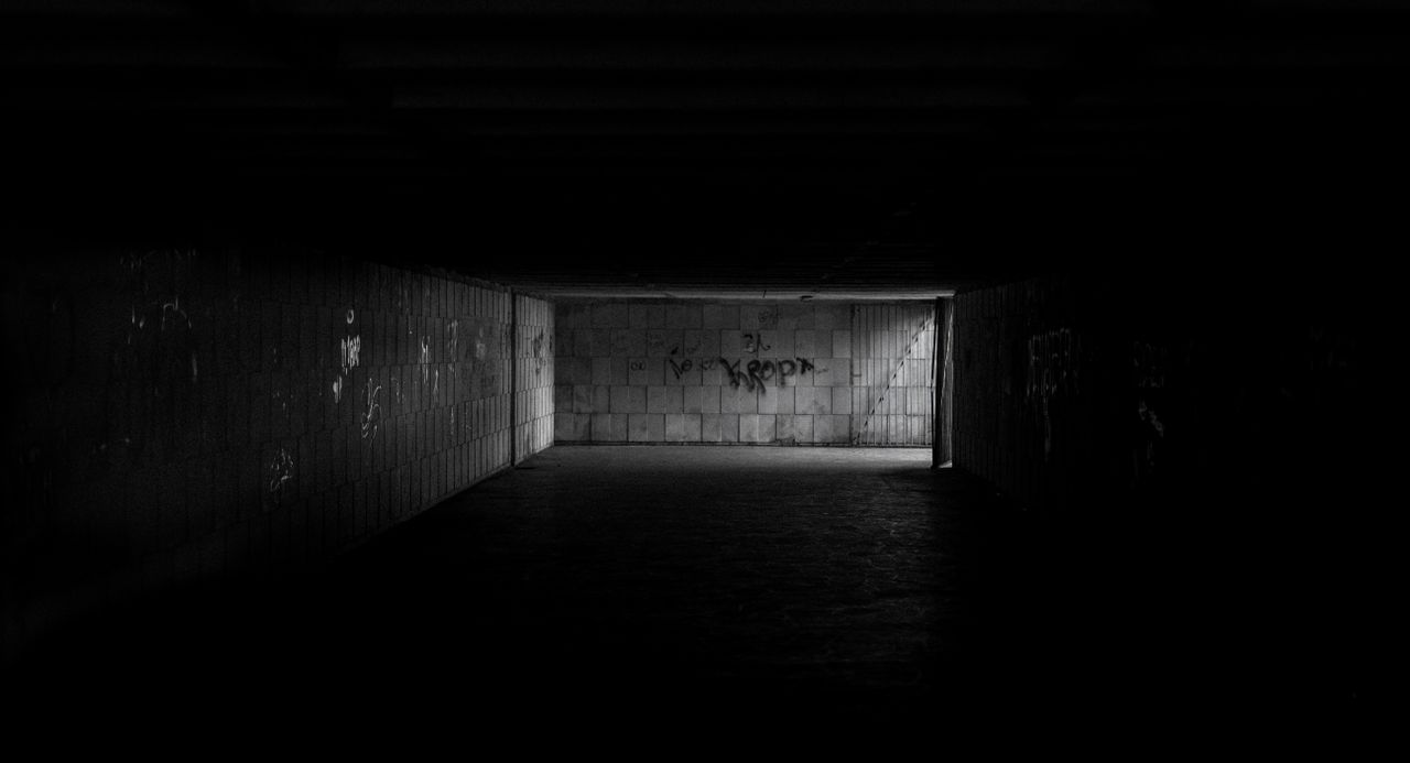 a dimly lit tunnel with graffiti and concrete walls evokes mystery and