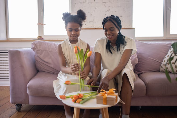 Mother And Daughter Arranging Flowers While Sitting On Sofa