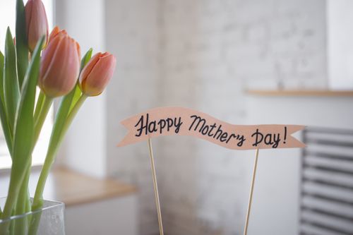 Free A beautiful arrangement of pink tulips with a 'Happy Mother's Day' sign indoors, perfect for celebration. Stock Photo