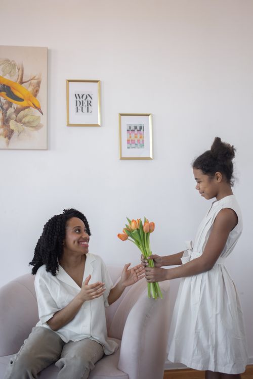 Free A joyful indoor scene of a daughter giving tulips to her mother, highlighting love and happiness. Stock Photo