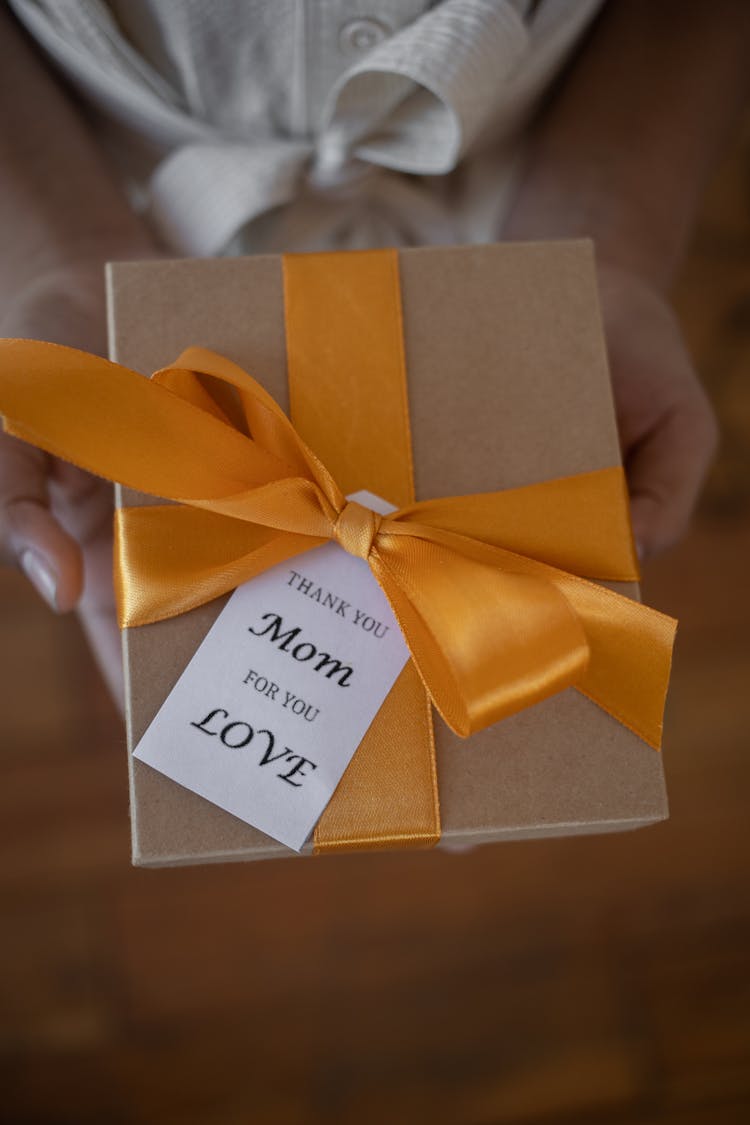 A Brown Carboard Box With Orange Ribbon And Gift Tag